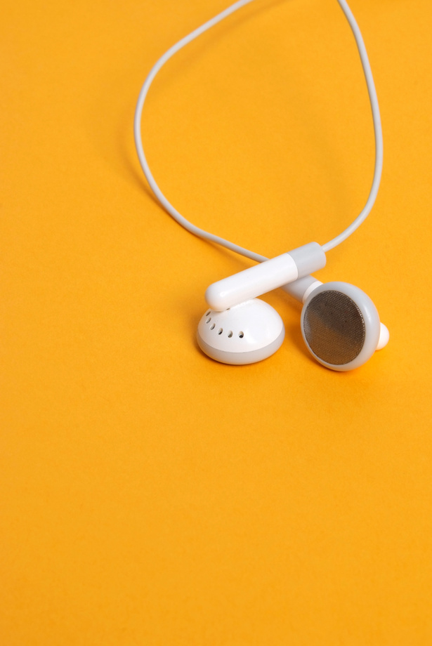 White corded ear buds against a solid yellow background.